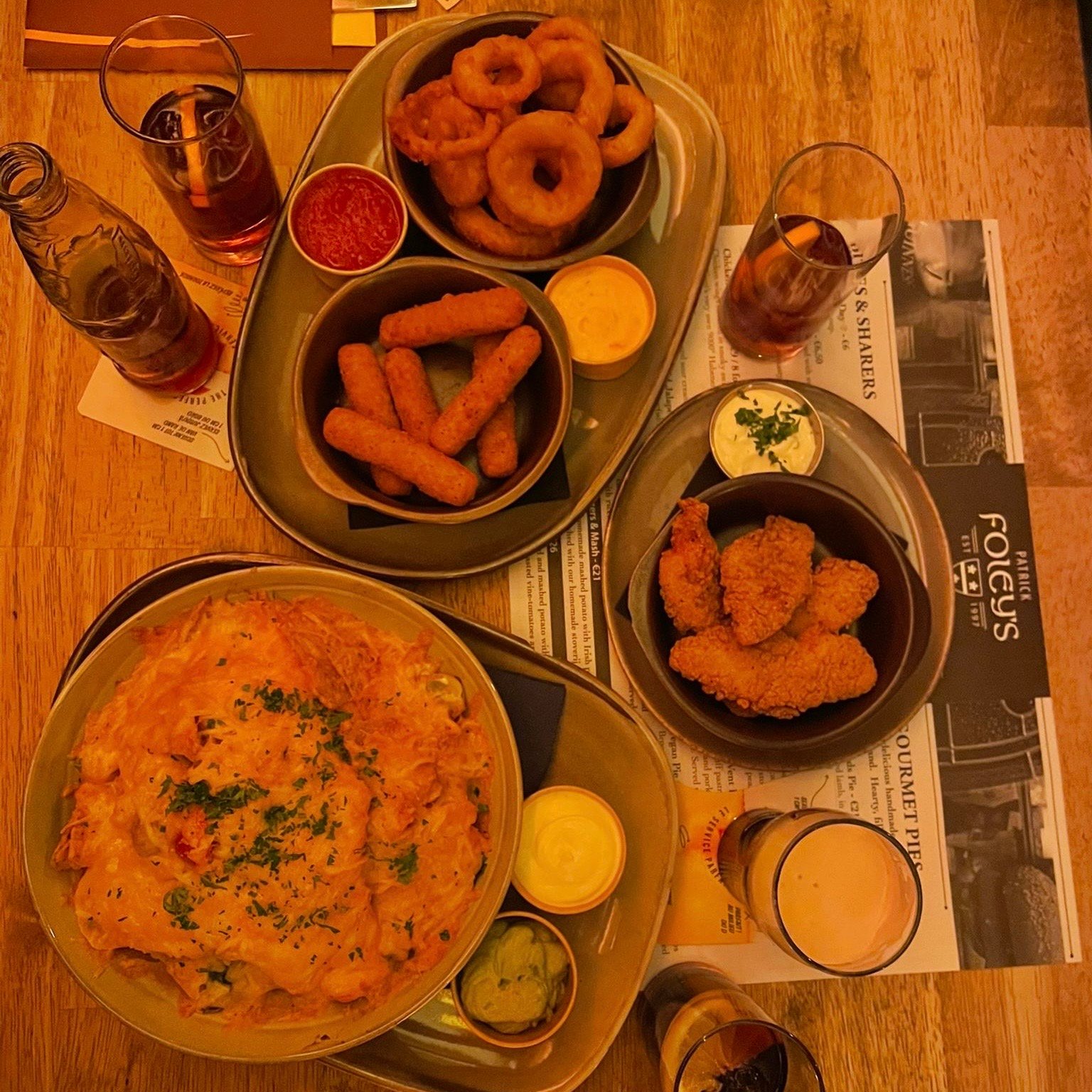 wooden table with nachos, chicken tenders, mozzarella sticks, onion rings, a lot of sauces and some drinks