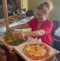 Employee at Shazanna carefully topping a fresh pizza.