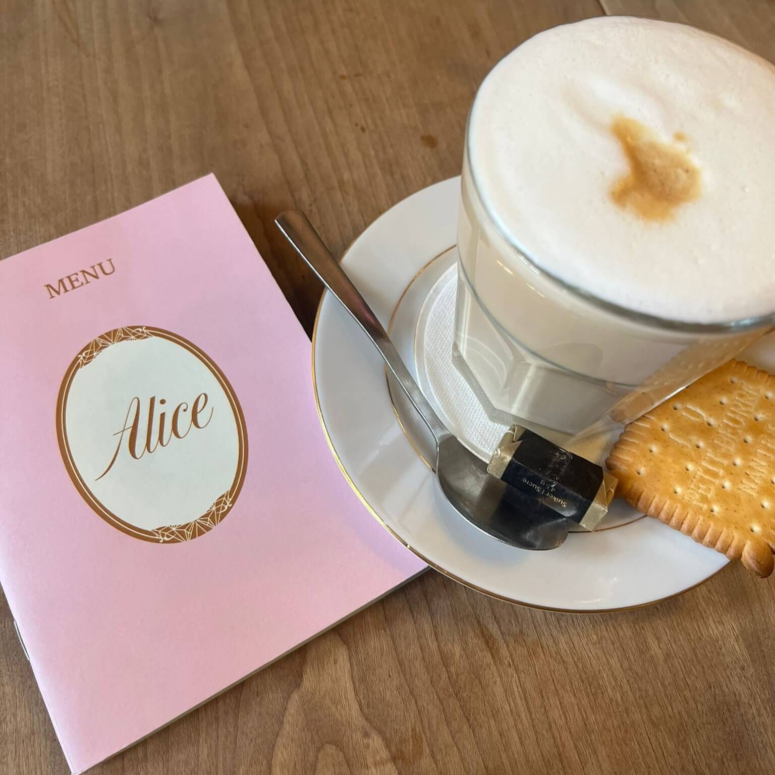 Menu of Alice with cappucino in a glass with a cookie.