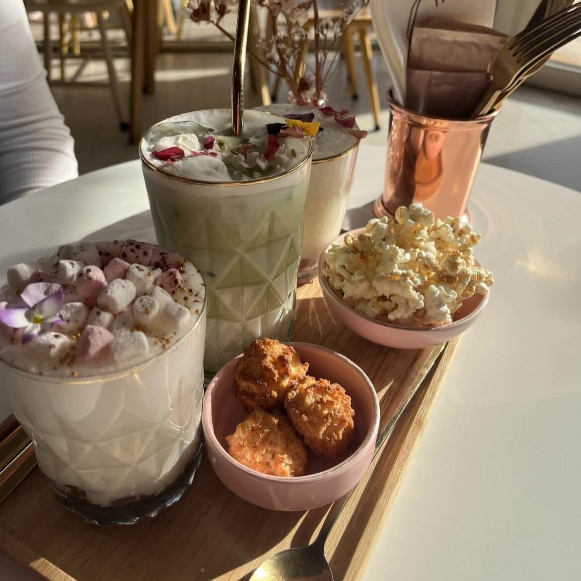 Coffee, hot chocolate and matcha on a plate with popcorn and coconut biscuits, all decorated with flowers