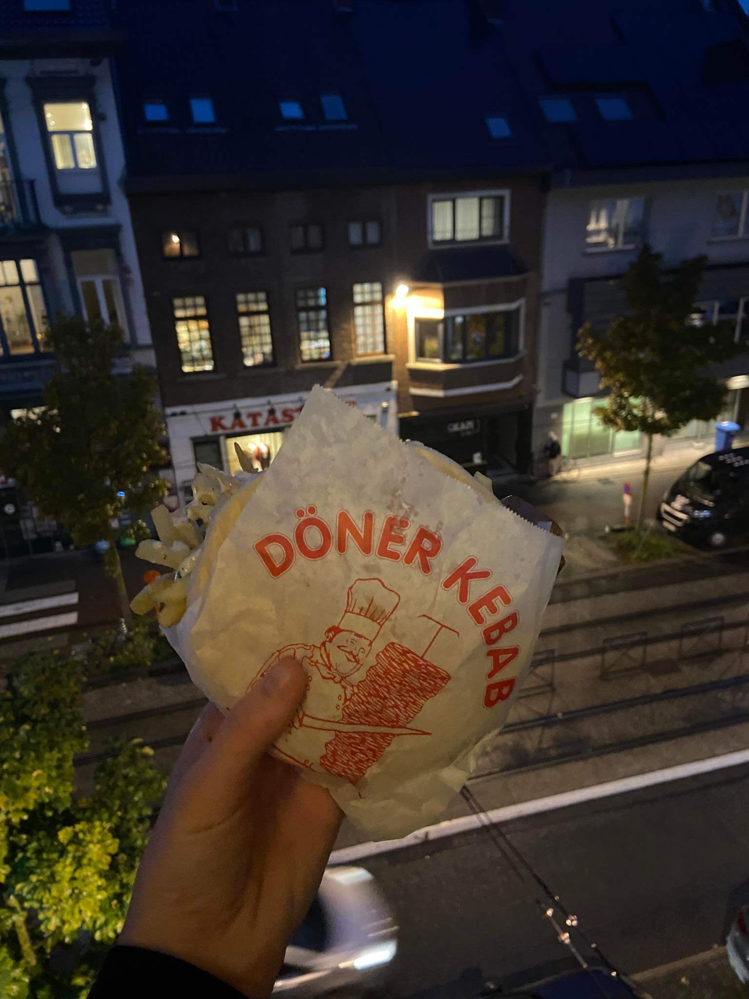 Urban comfort captured: Hand holds a wrapped pita on a balcony, a delightful moment with the lingering aroma of döner kebab.