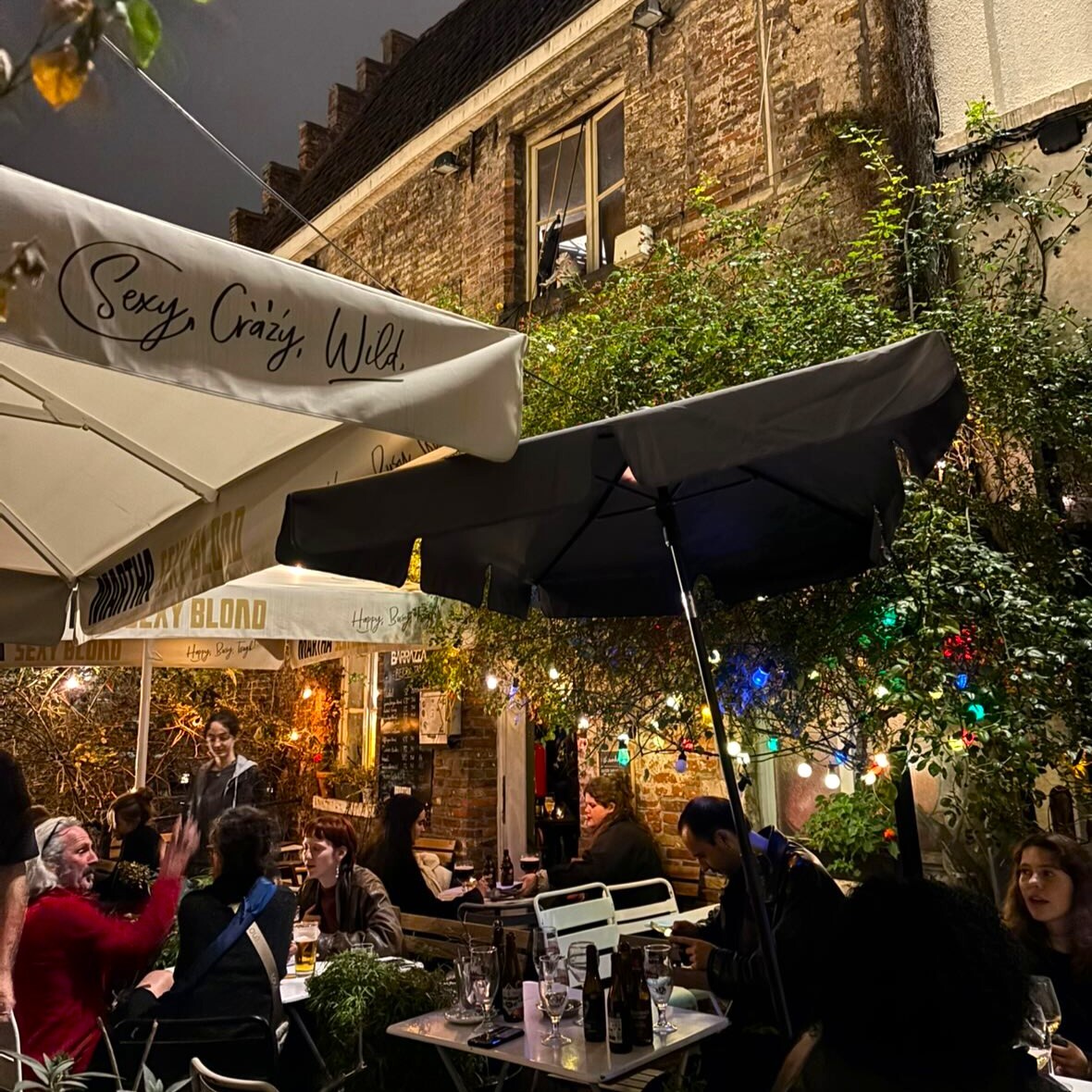 Terrace in a small street with parasols and colored lights. People are chatting to eachother.