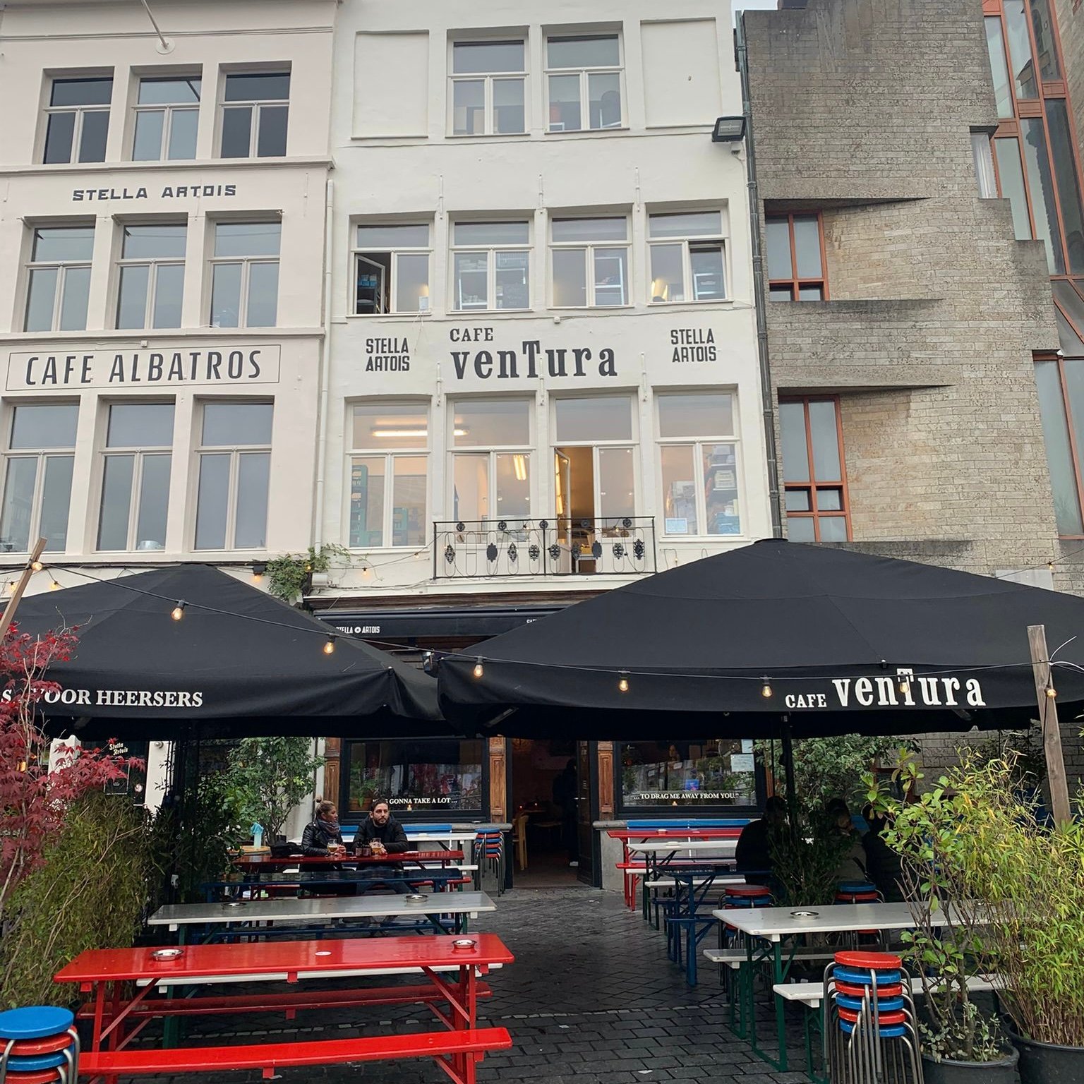 big white building with the name venTura, with two big black parasols and under them are red, white and blue tables and chairs