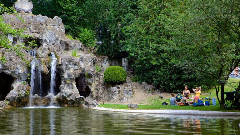 A pond with a waterfall and some people sitting on the grass