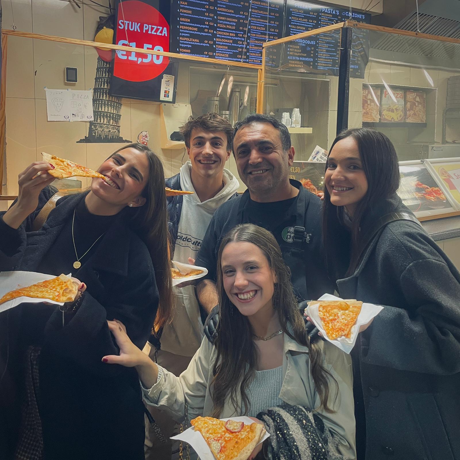 Group of students enjoying pizza slices with the chef at a takeaway place on Overpoortstraat, Gent.