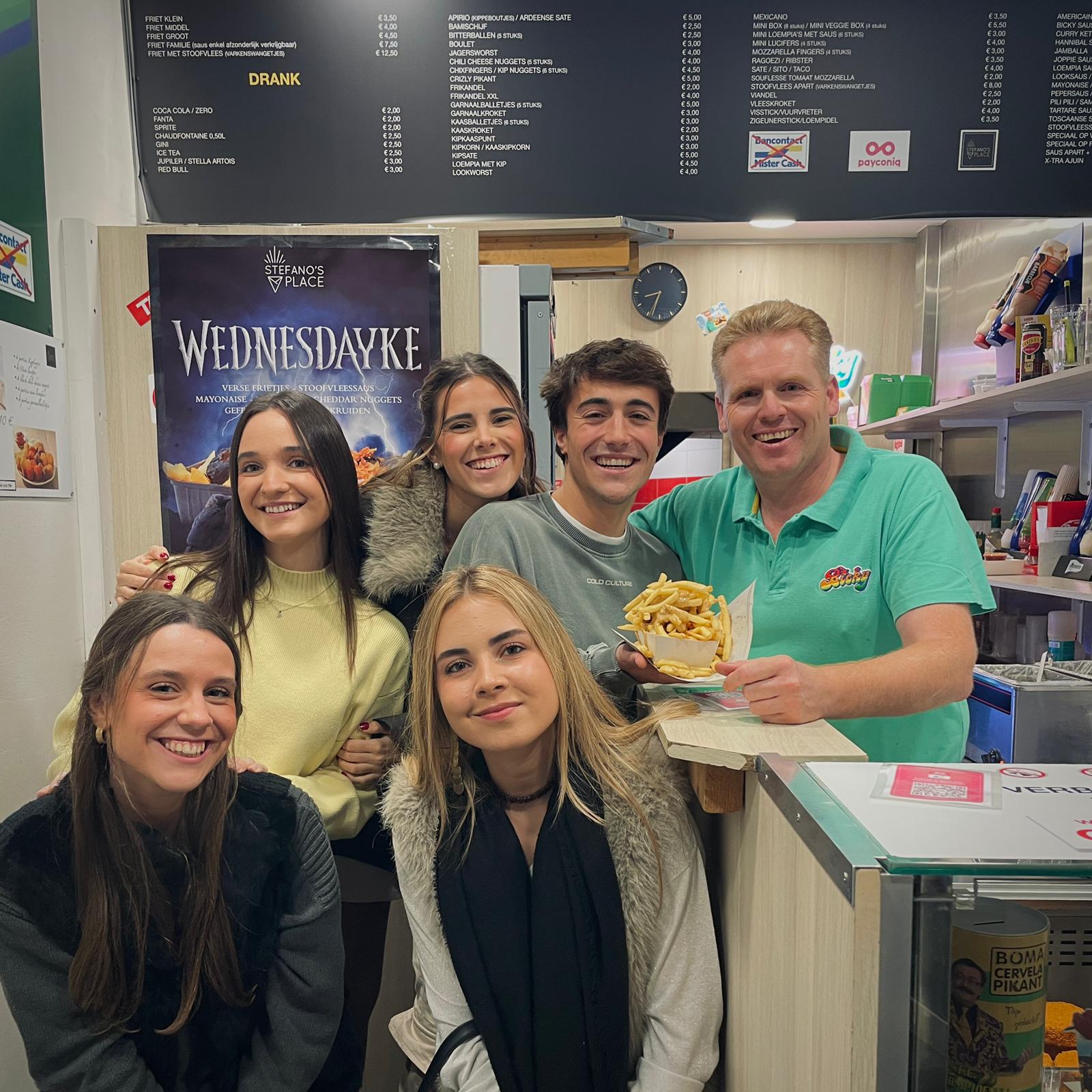 Erasmus students grabbing fries and posing with the friendly staff at a snack bar in Gent.
