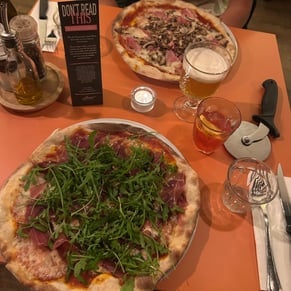 Two pizzas & two drinks on an orange table