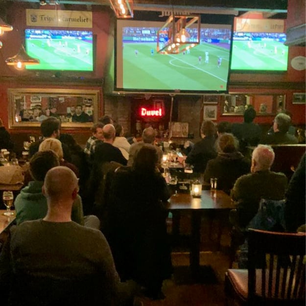 people sitting at tables and watching football on three different screens