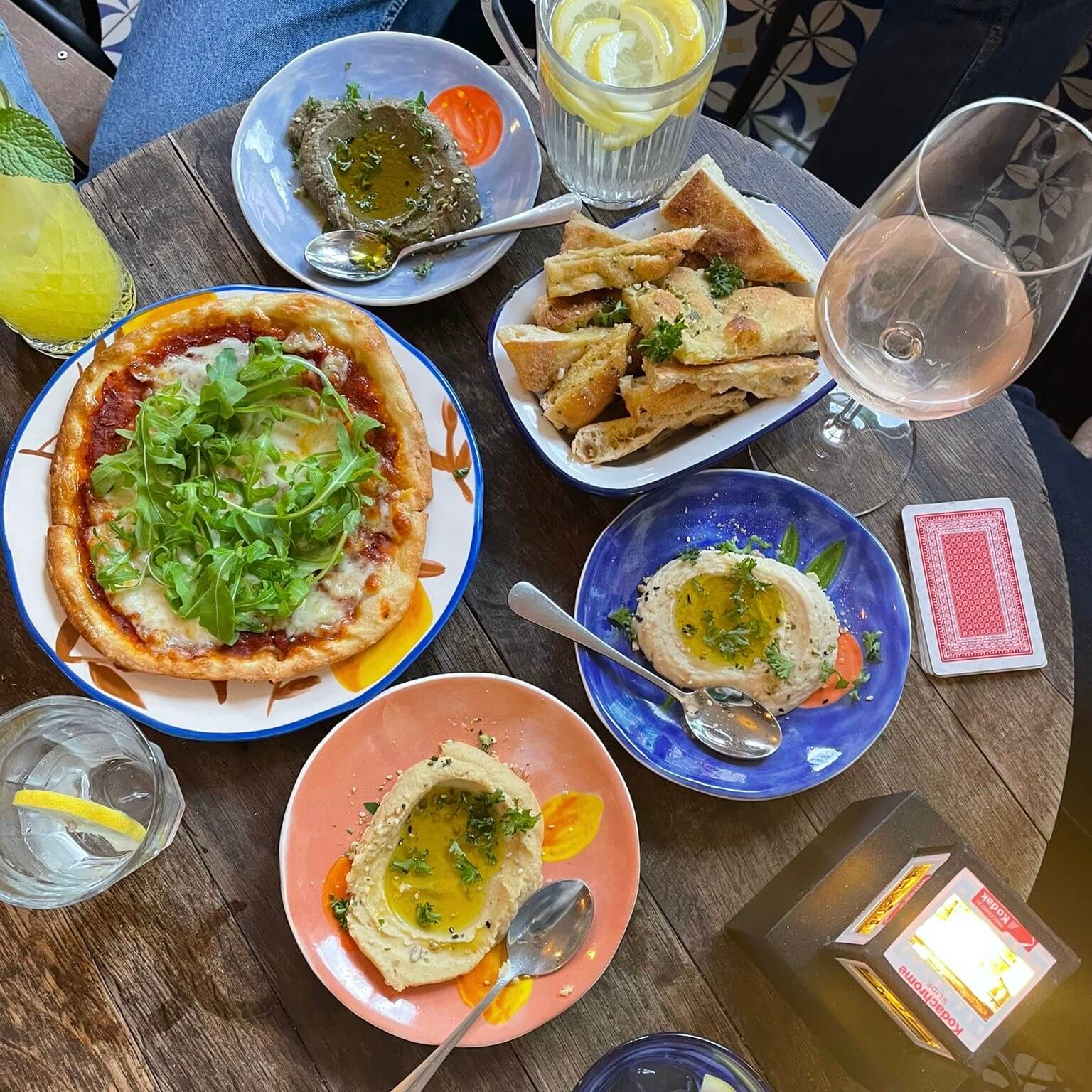 wooden table with mini pizza, three types of vegetable dip, focaccia and some glasses