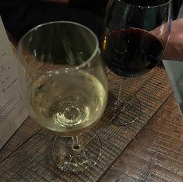 Two glasses of wine on a wooden table at OTOMAT in Ghent, creating a warm and cozy dining atmosphere.
