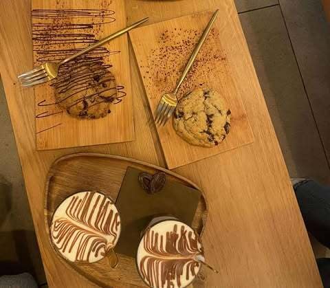 Two cookies on a wooden plate, with two cups of chocolate milk