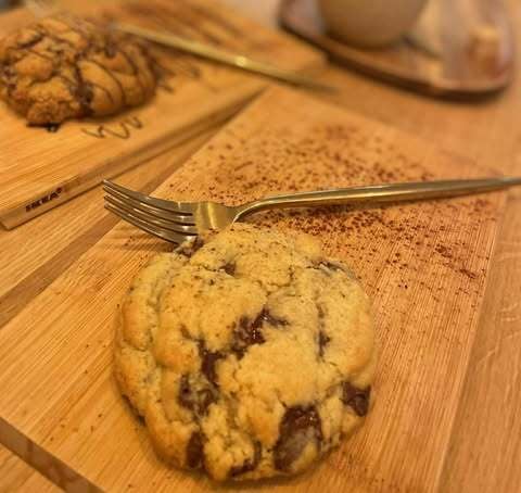 Chocolate chip cookie on a wooden plate, next to a golden fork