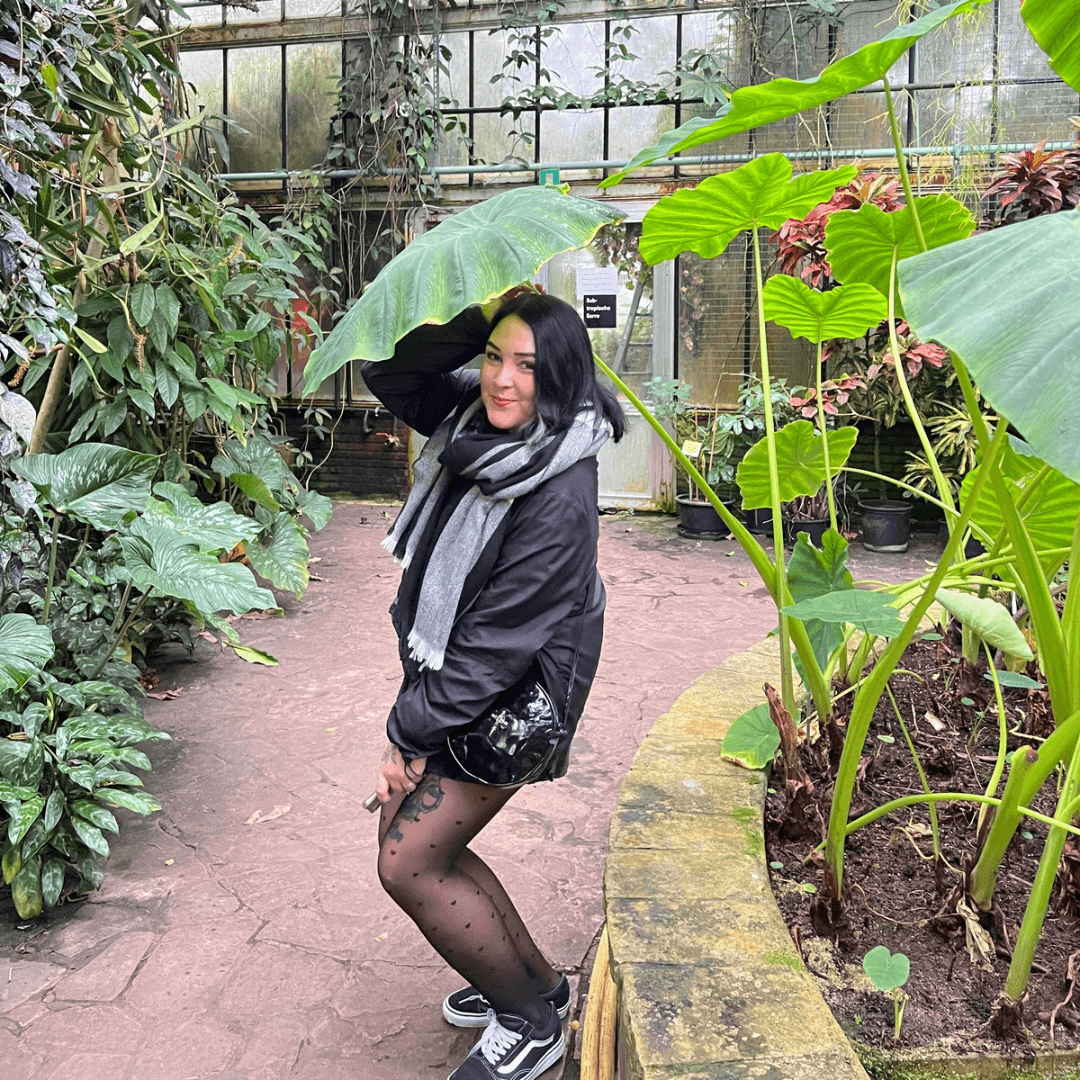 A woman is holding a plant which poses as an umbrella. She is surrounded by other plants.