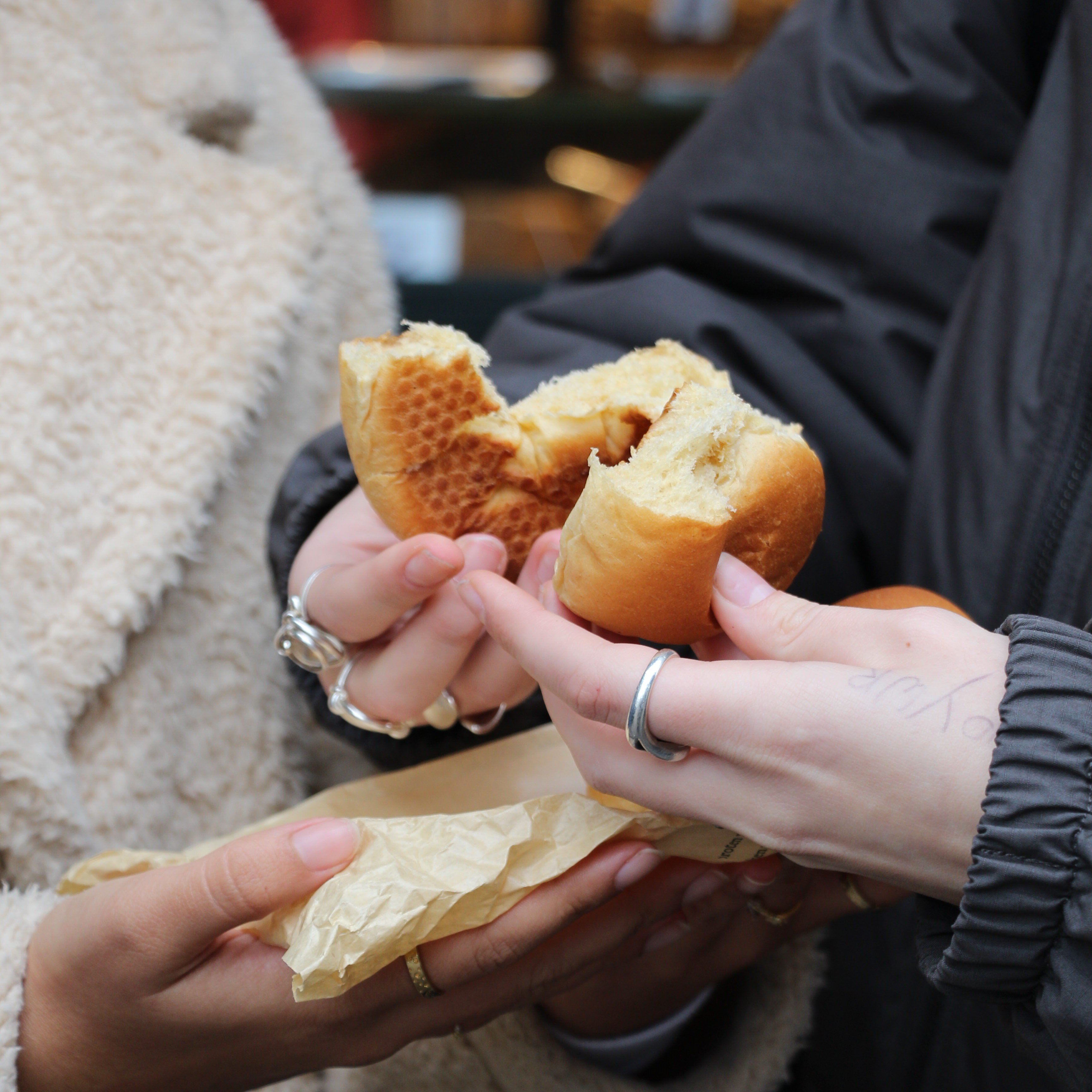 Hands breaking a *mastel* (traditional Ghent bread roll) in half.