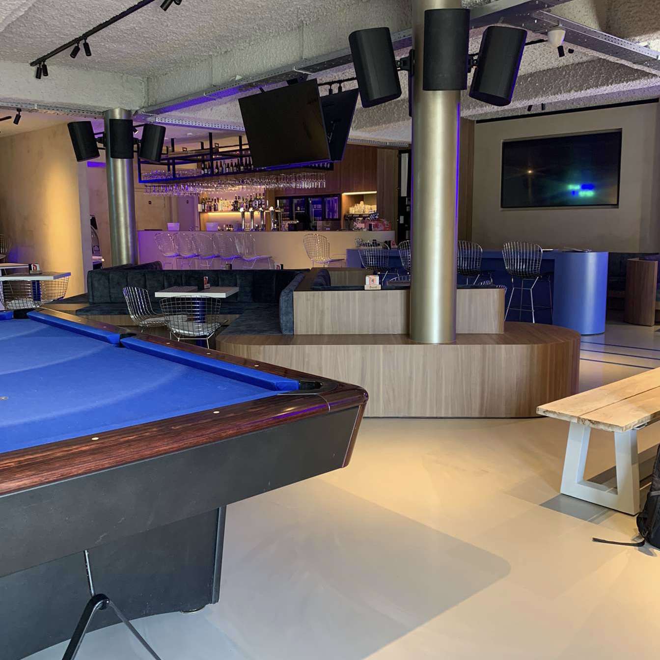 A pool-table in located in the middle of a bar with tv-screens