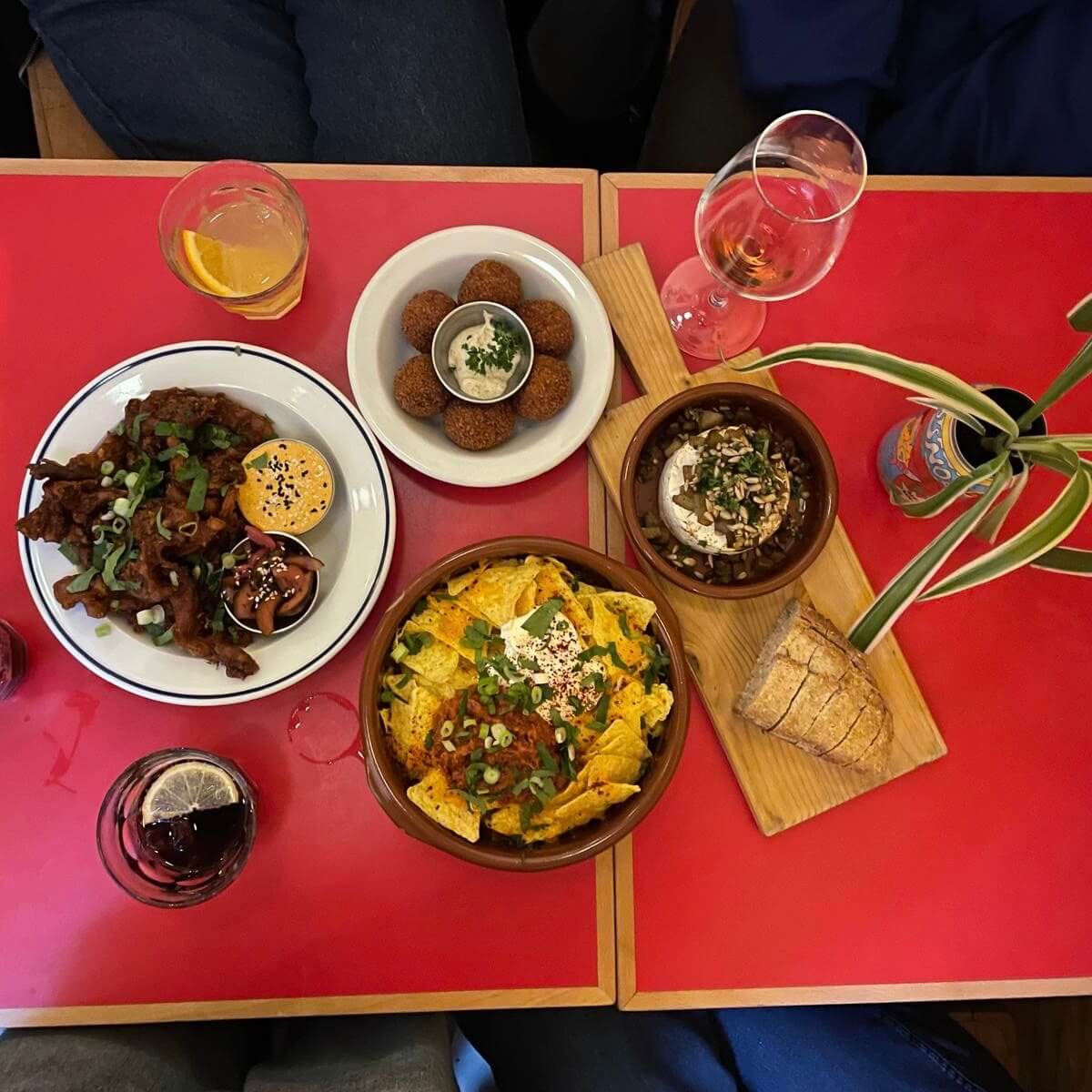 red table with nachos, tempura, bitterballs, baked camembert with bread slices and some glasses