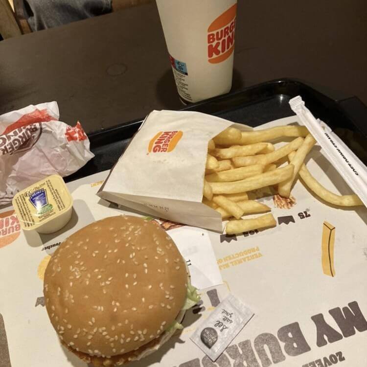 Crispy Chicken menu from Burger King, featuring a crispy chicken sandwich with lettuce and sauce, a side of golden fries, a refreshing soft drink, and a small container of dipping sauce