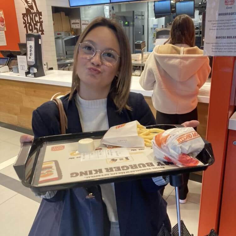 Yente holding a plate with a burger and fries in Burger King, walking towards her seat to enjoy her meal