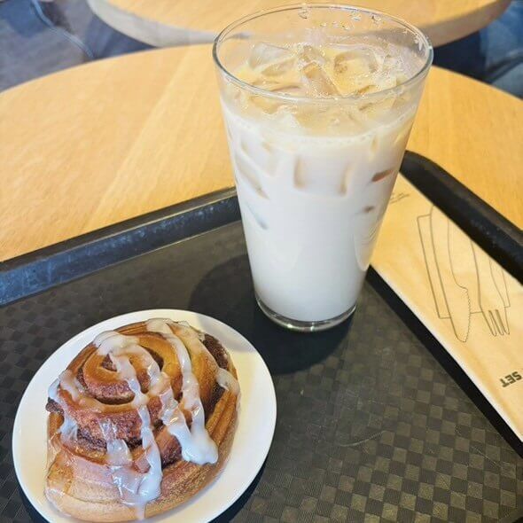 Starbucks iced latte in a clear glass with a straw, next to a freshly baked cinnamon roll on a plate